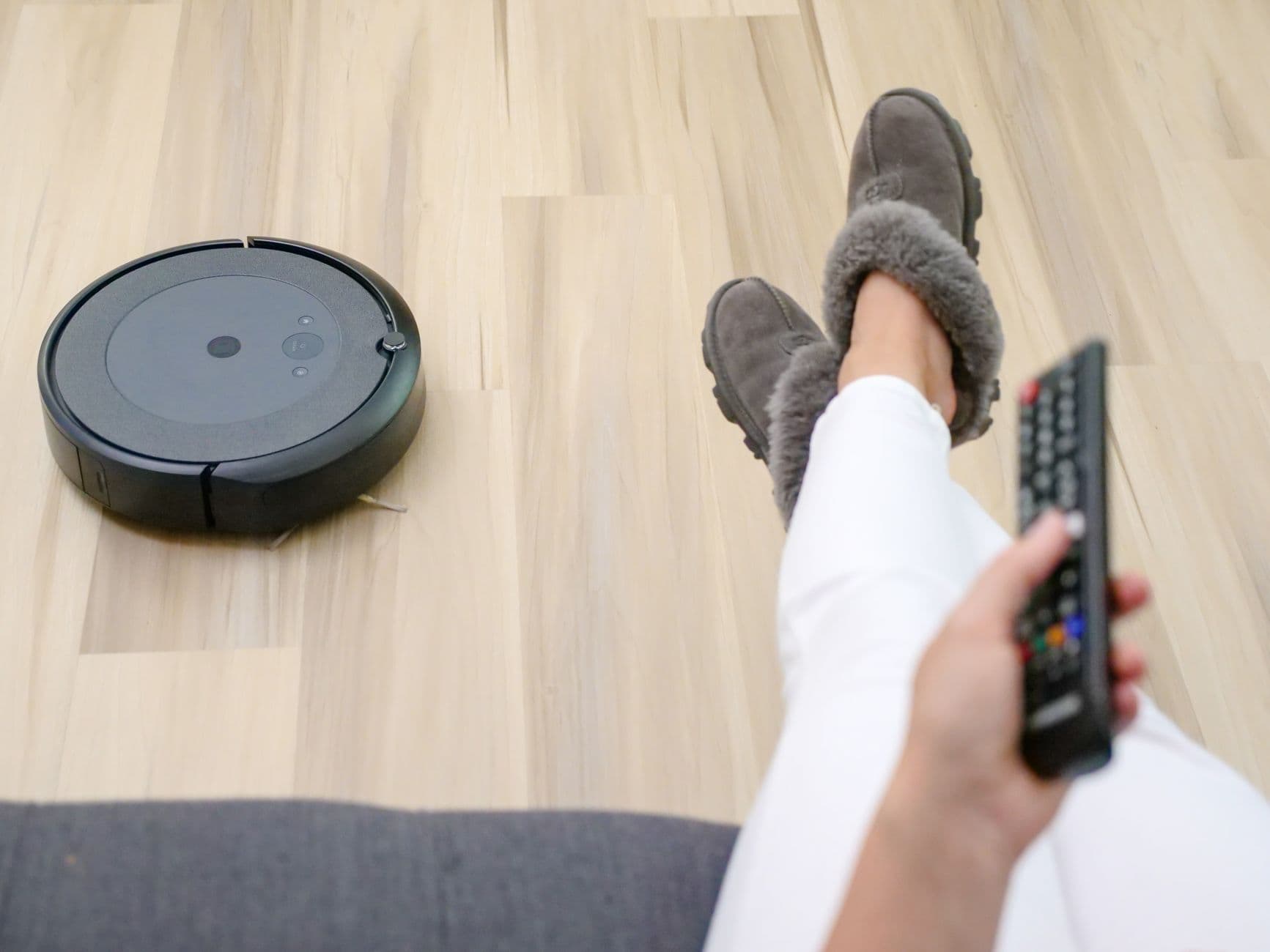 A robot vacuum cleaning a hardwood floor while someone relaxes on a couch