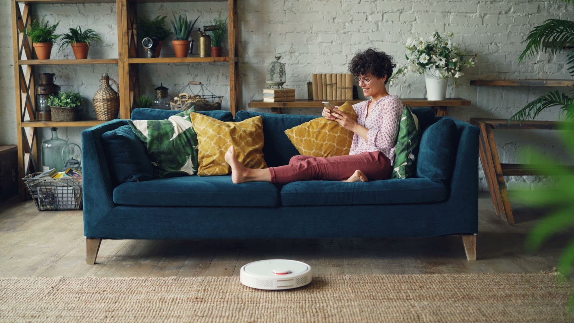 A robot vacuum cleaning a living room floor while someone relaxes on a sofa