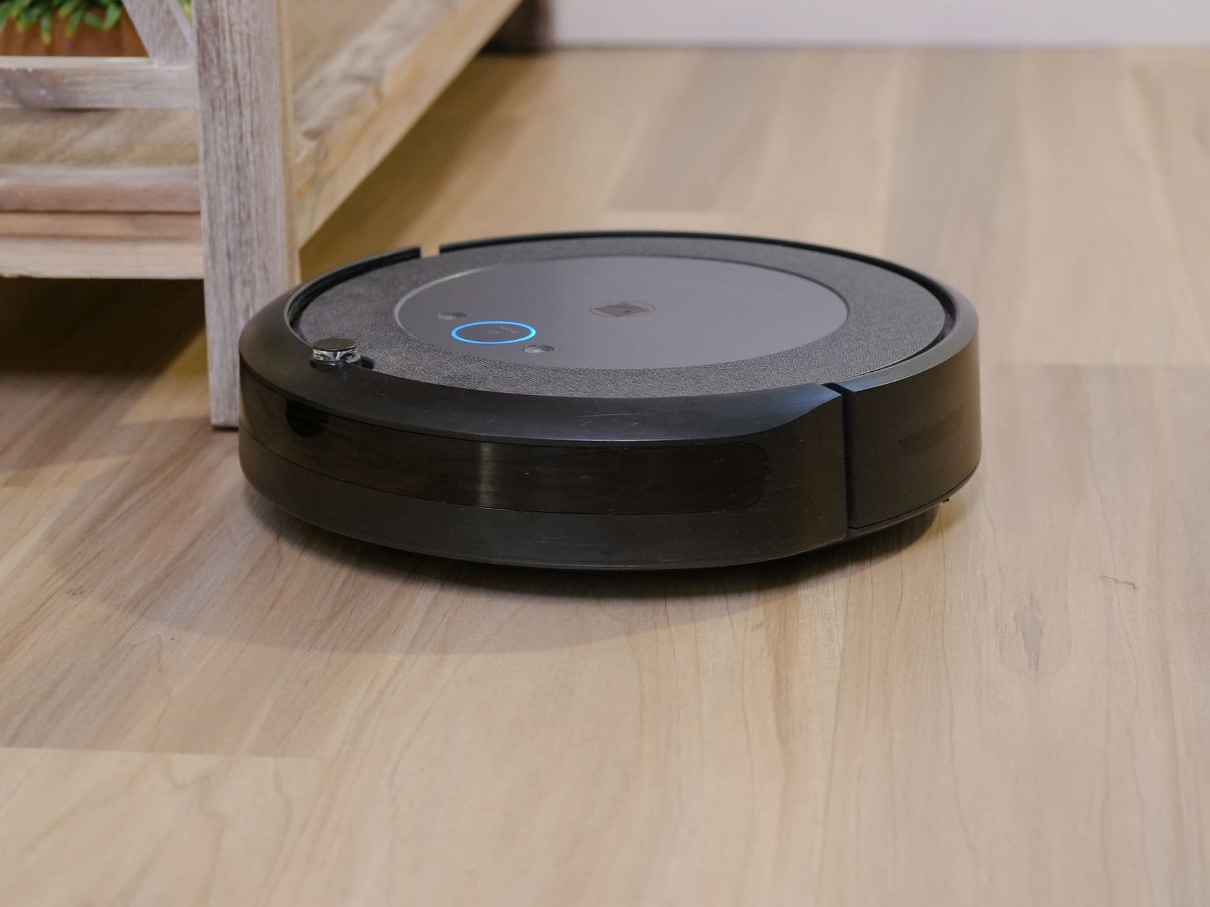 A robot vacuum moving across a wooden floor indoors