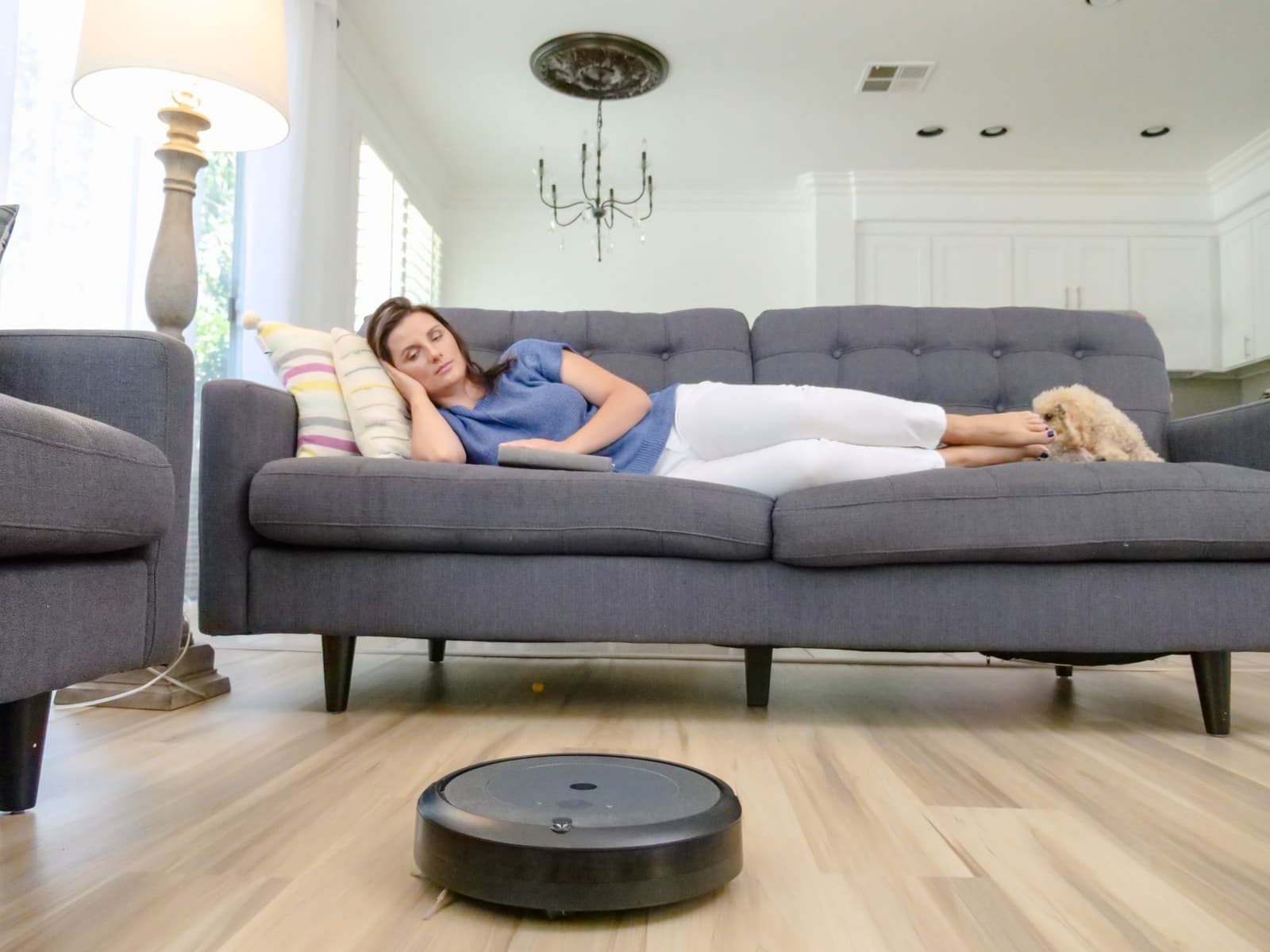 A person relaxing on a sofa while a robot vacuum cleans the hardwood floor