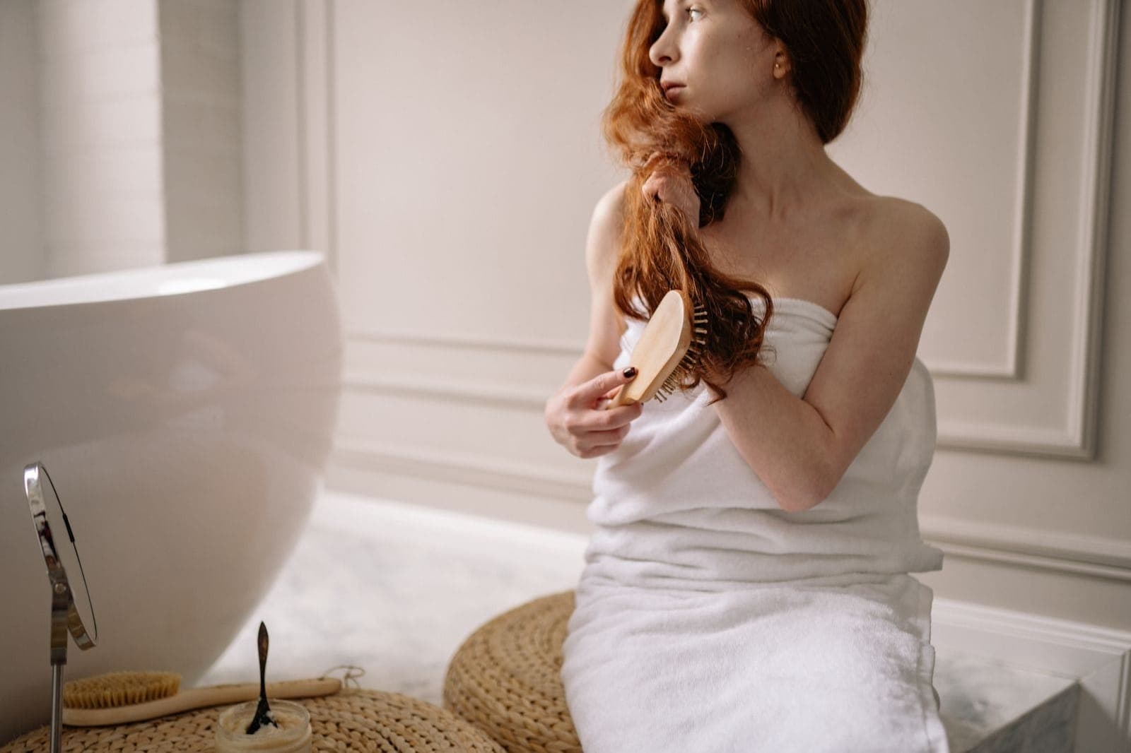 A person wrapped in a towel brushing long hair in a bright bathroom