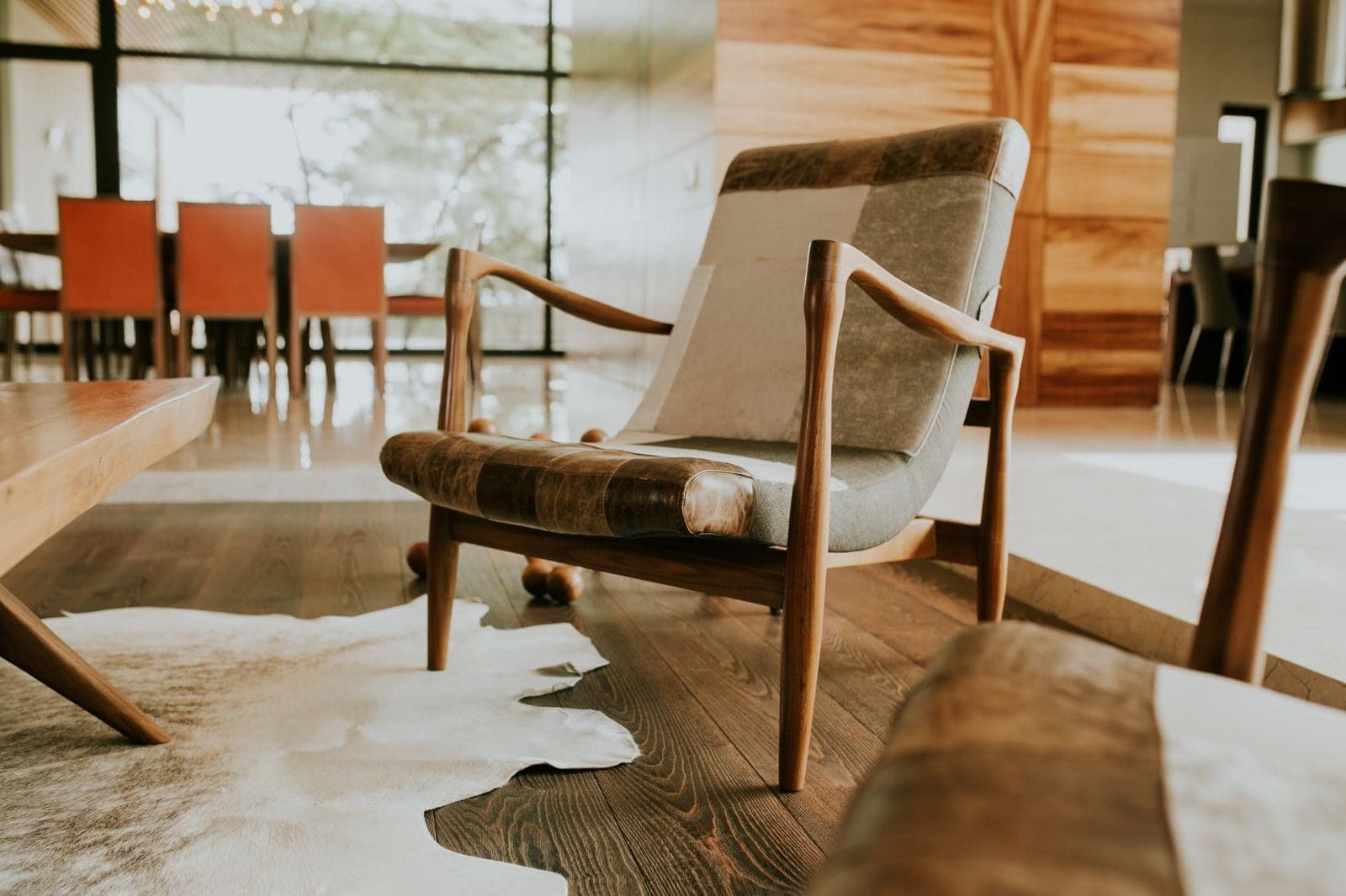 A hide rug meeting a dark wooden floor beside an armchair, with a dining table beyond
