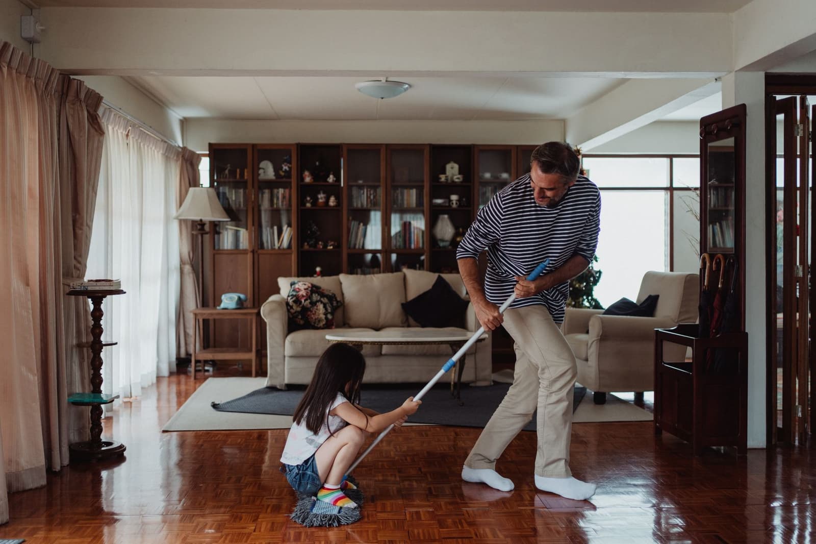 A parent and child cleaning the floor of a living room together