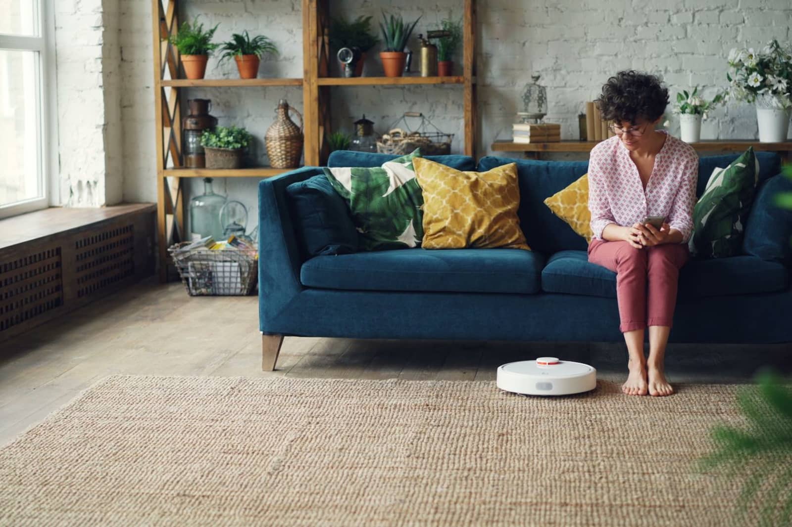 A white robot vacuum at the edge of a jute rug beside a sofa in a living room