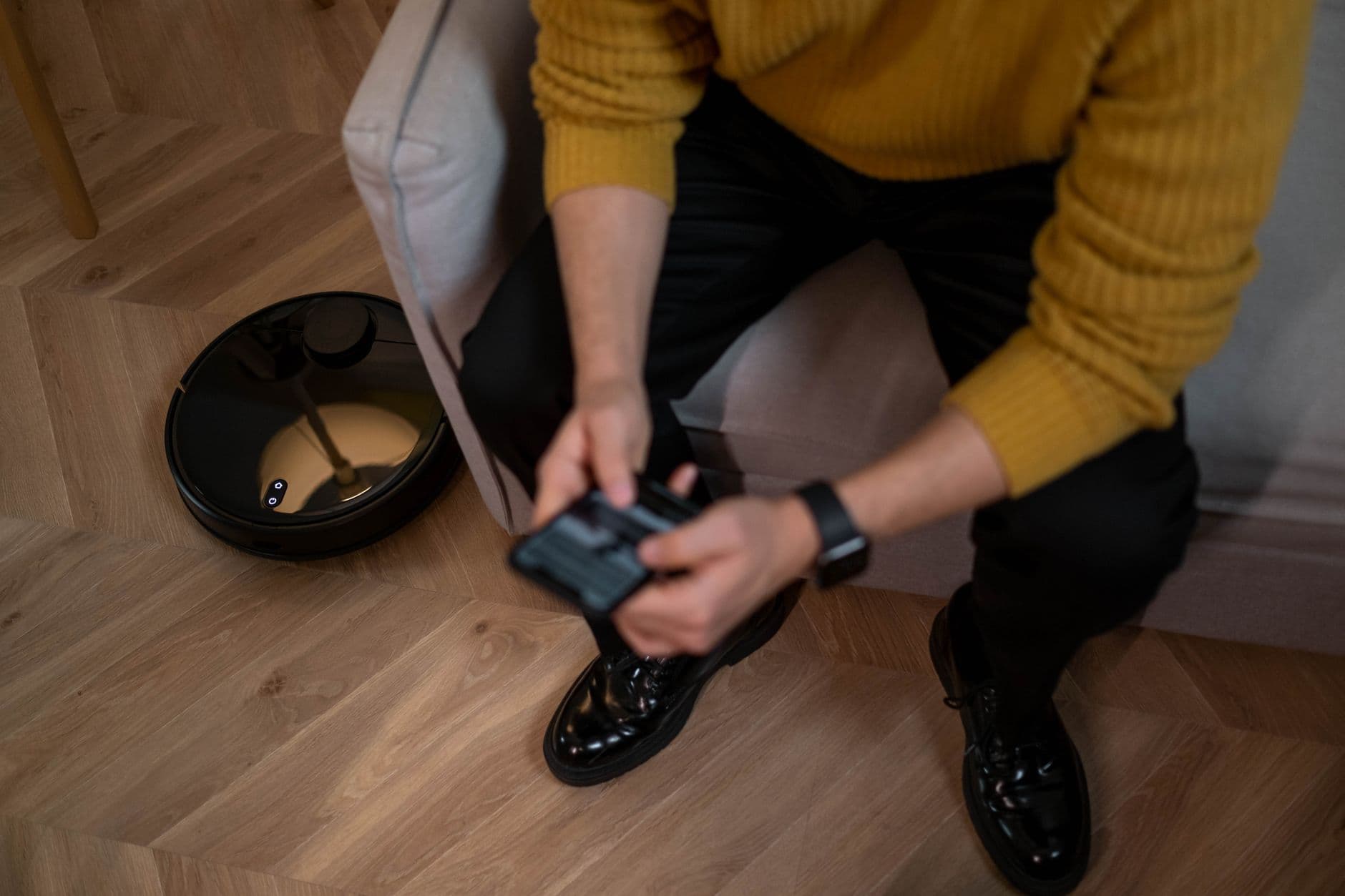 A person using a remote to control a robot vacuum on a wooden floor
