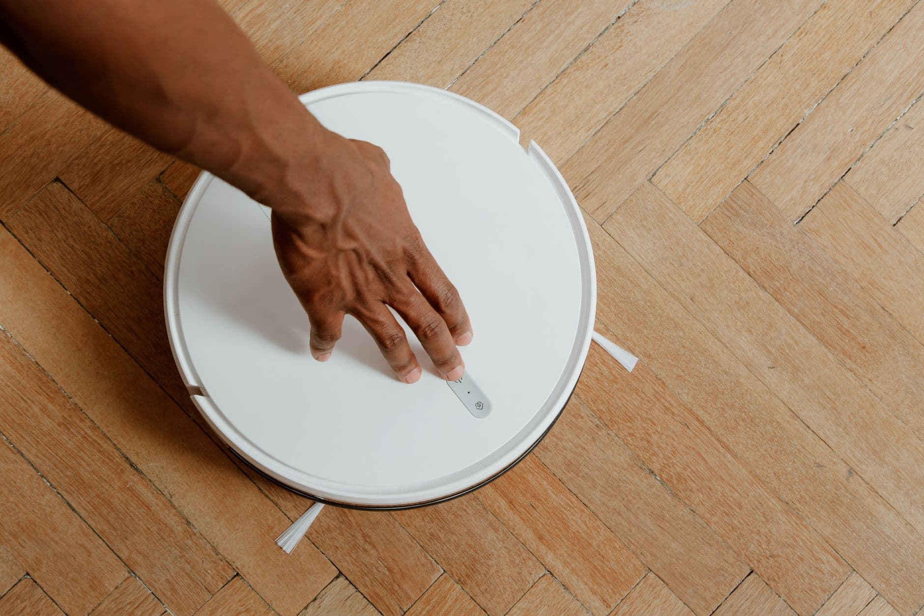 A hand activating a robot vacuum on a wooden floor