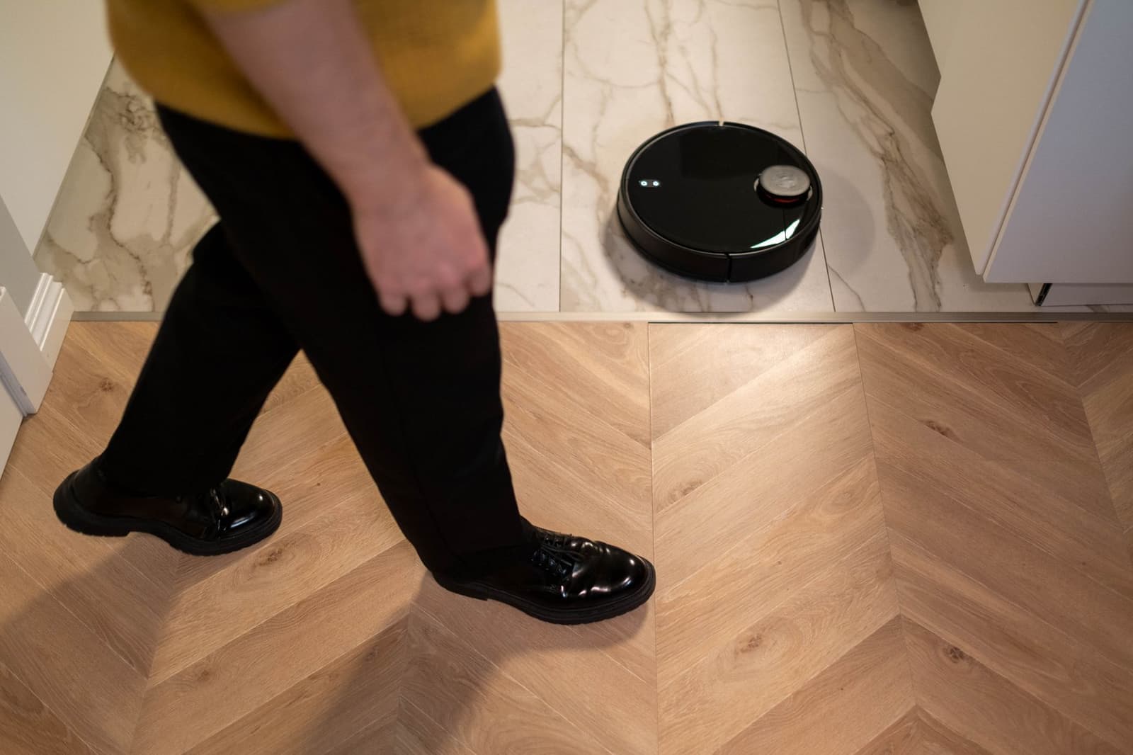 A robot vacuum on a wooden floor as someone walks past, seen from above