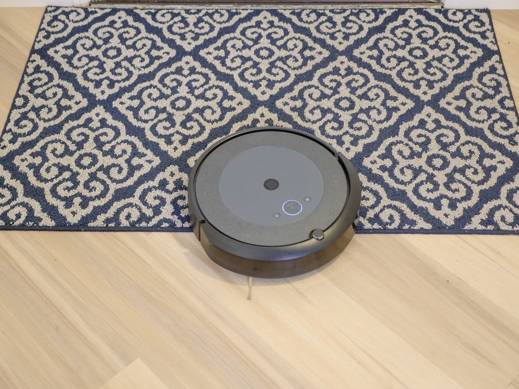 A robot vacuum cleaning a patterned carpet on a wooden floor