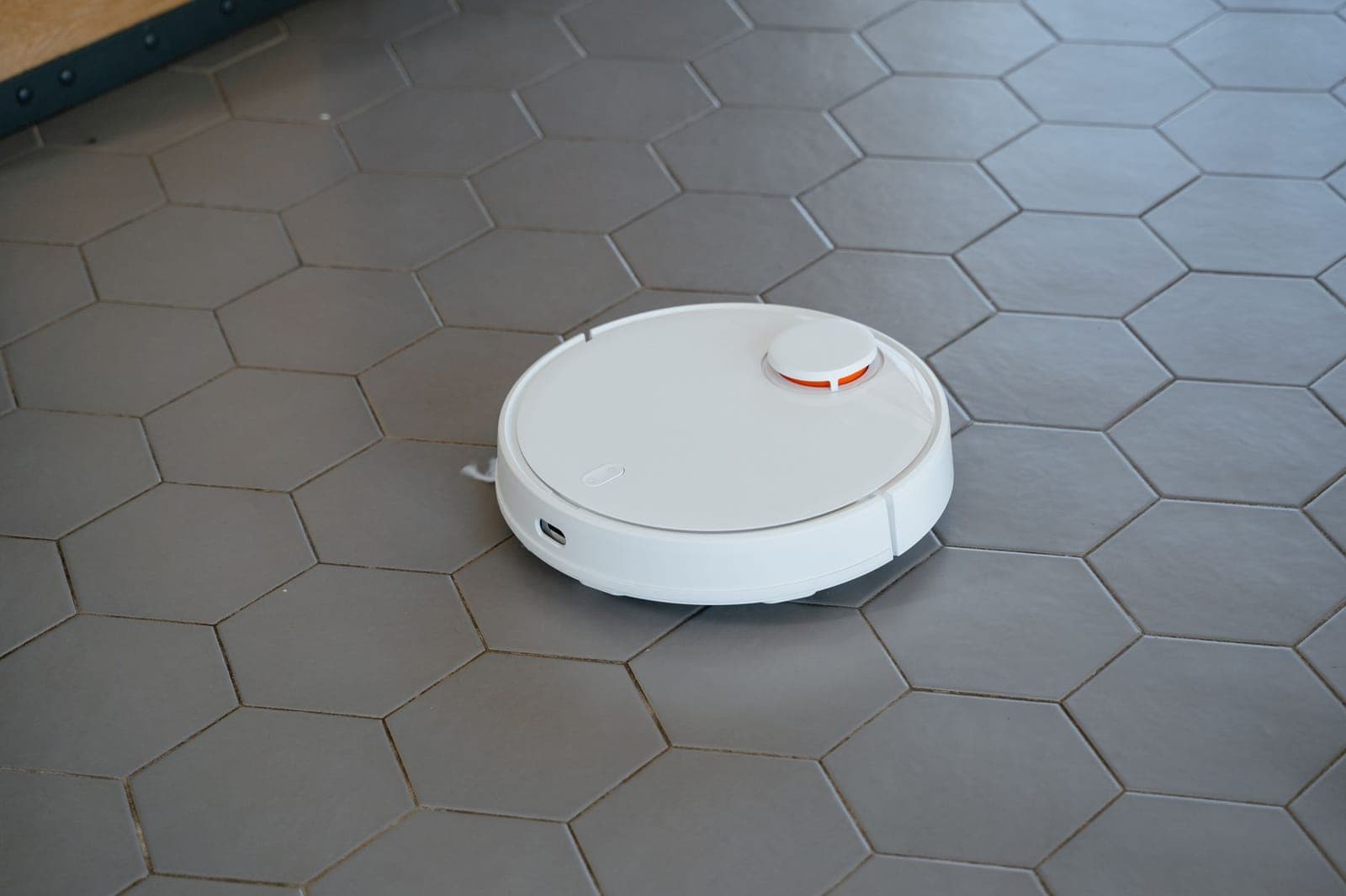 A white robot vacuum cleaning a hexagonal tiled floor
