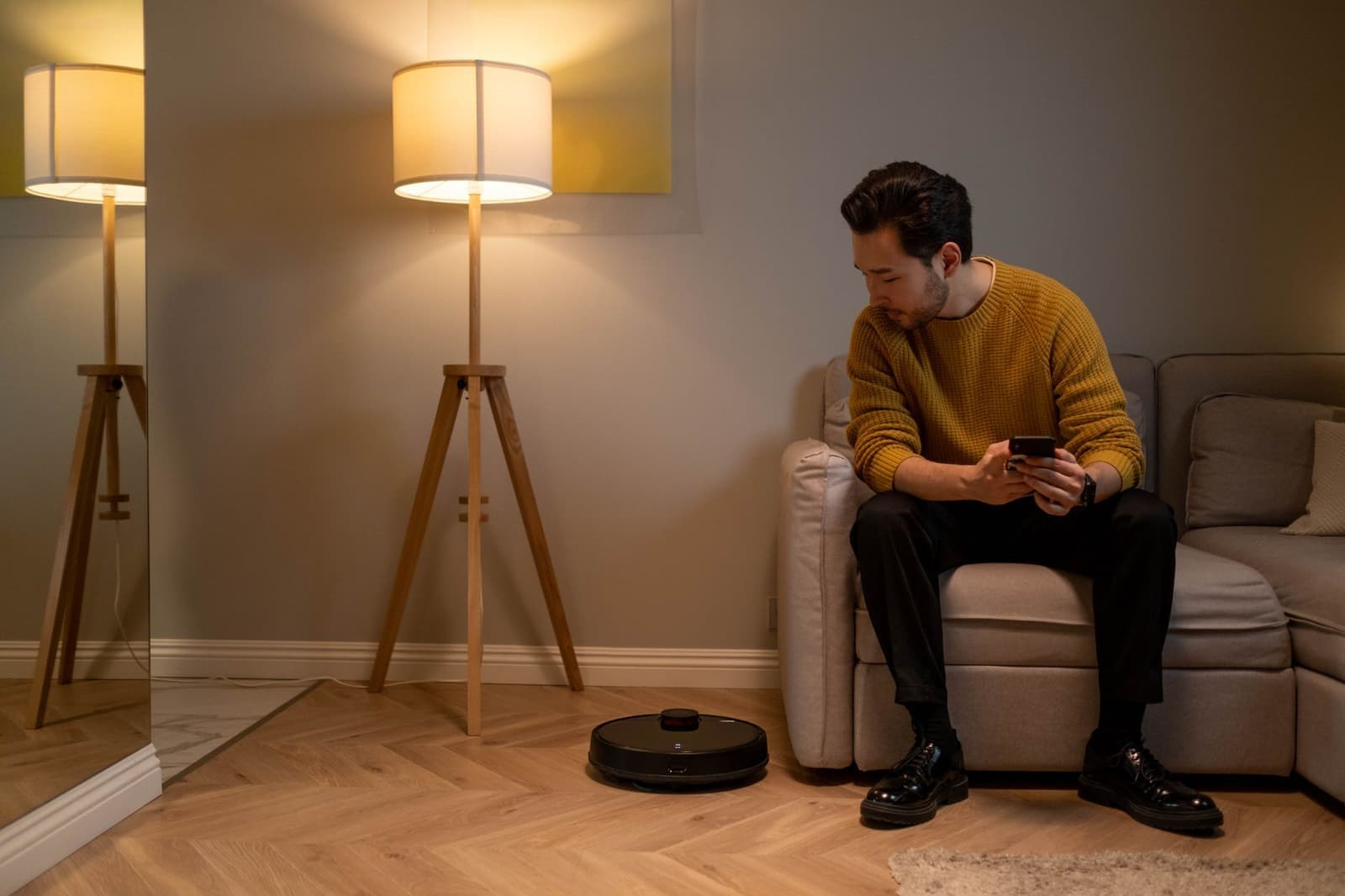 A person using a smartphone while a robot vacuum cleans a modern living room