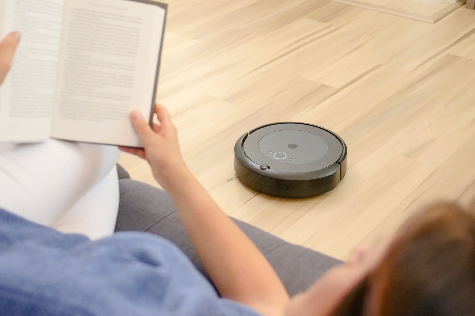A person reading on a sofa while a robot vacuum cleans the floor nearby